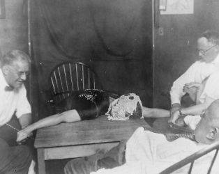 1925 photo Woman medium lying on table, with ectoplasm on her head 