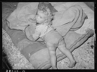 child of white migrant strawberry picker on bed in tent